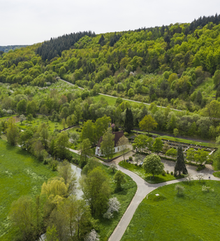 Luftbildaufnahem auf einen Parkplatz/Wohnmobilstellplatz bei Distelhausen. Daneben ist eine Kapelle und ein Friedhof zu sehen.  Es ist ein idyllischer Ort an der Tauber, mit Wiesen und bewaldeten Hügeln. | © Tourist-Info Tauberbischofsheim
