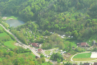 Luftbildaufnahme auf den im Tal gelegenen und mit vielen Bäumen bepflanzten Campingplatz Romantische Strasse in Creglingen-Münster. Der Hang ist bewaldet und im Hintergrund ist ein kleiner See zu sehen. | © Liebliches Taubertal