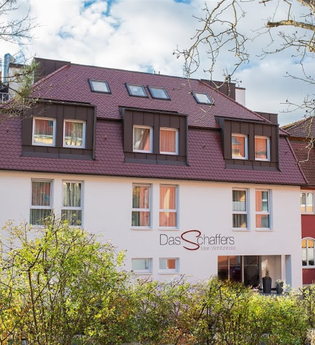 Hotel Das Schaffers mit rotem Dach und weiß-roter Fassade, umgeben von Bäumen und Sträuchern | © Das Schaffers