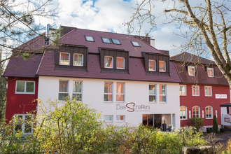 Hotel Das Schaffers mit rotem Dach und weiß-roter Fassade, umgeben von Bäumen und Sträuchern | © Das Schaffers