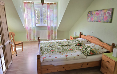 Schlafzimmer mit Doppelbett mit floral gemusterten Bettdecken, Holzmöbeln, Fenster mit bunten Vorhängen und grün gestrichener Wand | © Familie Fuhrmann