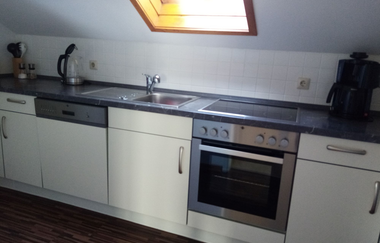 weiße Küchenzeile mit Herd, Spülmaschine und Spülbecken unterm Fenster