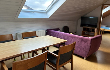 Blick in den Aufenthaltsraum mit großen Esstisch, lilaner Couch und Fernseher | © Neckar-Zaber-Tourismus e.V.