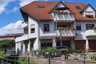 Mehrstöckiges Wohn- und Geschäftshaus mit rotem Ziegeldach und Balkonen mit Blumen, darunter die Sankt Urban Apotheke | © Ferienwohnung Roth