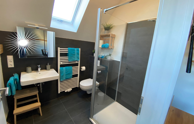 Modernes Badezimmer mit Dusche, weißem Waschbecken, Wand-WC, Handtuchheizkörper mit blauen Handtüchern und Dachfenster | © Ferienwohnung Etzl