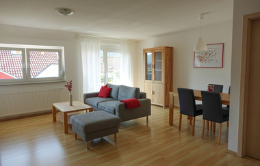 Wohn und Esszimmer mit grauer Couch und Couchtisch, einem Esstisch mit vier Stühlen und einer Schrankvitrine | © Neckar-Zaber-Tourismus e.V.