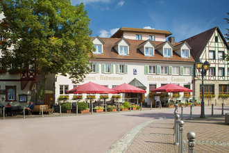 Frontansicht des Hotels vom Marktplatz aus. Vor dem Hotel sind Sonnenschirme aufgestellt. | © Flair Hotel Weinstube Lochner