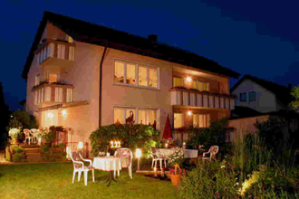 Ein großes Haus mit einem Garten, Gartenmöbel stehen dort. Es ist Abend. | © Gästehaus Marianne