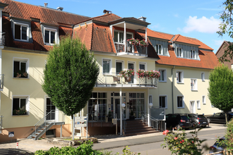 Mehrstöckiges Hotel mit gelber Fassade, roten Dachziegeln, Balkonen mit Blumen und parkenden Autos davor | © Hotel Alexa
