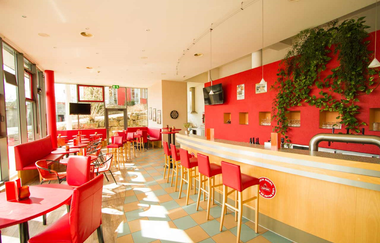 Helle Bar mit roten Stühlen und Tischen, langer Holztheke, roten Wandnischen und grünen Pflanzen an der Wand | © Savoy Hotel