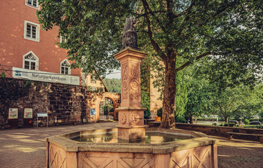 Brunnen aus Buntsandstein. Im Hintergrund ein rotes Haus mit einem Baum. Eberbach im Odenwald | © Touristikgemeinschaft Odenwald e.V.