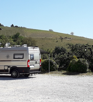 Wohnmobil auf einem Schotterplatz bei gutem Wetter mit Weinbergen im Hintergrund | © Unbekannt