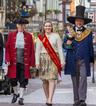 Eine Gruppe von fünf Personen in historischen Kostümen geht eine gepflasterte Straße entlang. Sie tragen Hüte, Mäntel und eine Schärpe. | © Stadt Besigheim