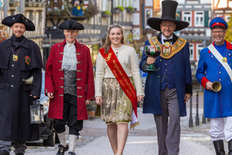 Eine Gruppe von fünf Personen in historischen Kostümen geht eine gepflasterte Straße entlang. Sie tragen Hüte, Mäntel und eine Schärpe. | © Stadt Besigheim