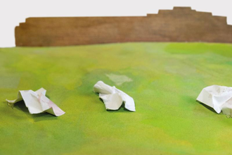 Drei zerknüllte weiße Zettel auf grünem Untergrund vor braunem Hintergrund.