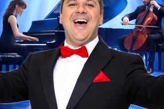 Ein Mann im Smoking steht vor einem Flügel auf einer Bühne mit dem Schriftzug 'Andrea Bocelli Tribute'. | © Andrea Bocelli Tribute