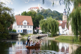 Ein Stocherkahn mit mehreren Personen fährt auf einem Fluss, im Hintergrund sind Gebäude und ein Turm zu sehen. | © Stadtverwaltung Vaihingen an der Enz