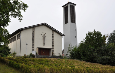 Weiße Kirche mit freistehendem Kirchturm an einem begrünten Hang