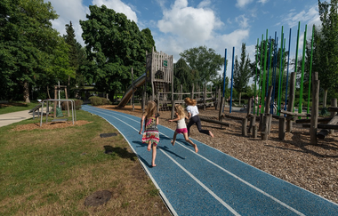 Drei Kinder rennen auf der blauen Laufbahn in der alla hopp-Anlage