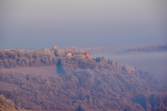 Luftbildaufnahme mit Blick auf die Burg Neuhaus in Igersheim. Die Burg steht auf einem Berg und ist von Wald umgeben. Im Tal ist Nebel zu sehen. | © Liebliches Taubertal