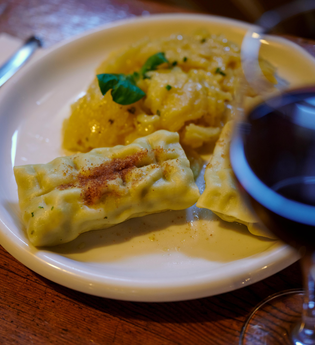 Ein Teller mit Maultaschen und Kartoffelsalat, daneben ein Glas Rotwein auf einem Holztisch. | © Kraichgau-Stromberg Tourismus e.V.