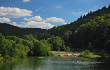 Blick auf den zwischen Wald und Bäumen gelegenen Münster-Badesee. Es sind viele Gäste im Wasser und auf der Liegewiese zu sehen. | © Tourist-Information Creglingen