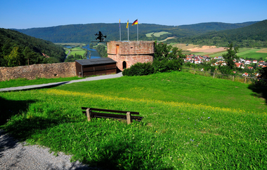 Blick auf den Turm mit Hexe bei der Freudenburg. Im Hintergrund ist Freudenberg, im Vordergrund eine Bank mit Wiesezu sehen. | © Liebliches Taubertal