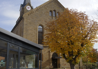 Blick auf die Westseite der Mauritiuskirche. Vor dem Eingang steht ein Baum mit bunten Blättern. | © Neckar-Zaber-Tourismus