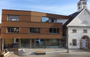 Außenansicht der Tourist-Information über den Obertorplatz. Das Gebäude hat eine moderne Holzfassade sowie eine große Glasfront. Rechts neben der Tourist-Info ist das Theodor-Heuss-Museum zu sehen. | © Neckar-Zaber-Tourismus e.V.