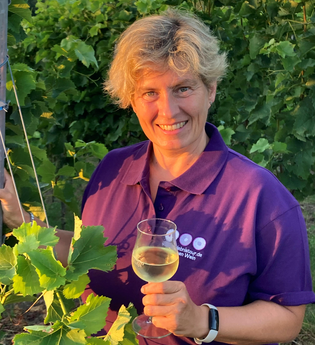 Nicole Betz mit lila Shirt der WeinErlebnisFührer und Weinglas in der Hand zwischen Weinreben | © Nicole Betz