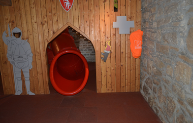 Blick auf einen Rutschenausgang in der Spielscheune in Röttingen. Der Ausgang ist mit einer Holzwand verkleidet. Ein gemalter Ritter hält daneben Wache. | © Tourismusverband "Liebliches Taubertal" e.V.
