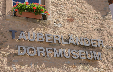 Blick auf den aus einzelnen Metallbuchstaben zusammengesetzen Namen "Tauberländer Dorfmuseum", der auf der Außenseite des Museums angebracht ist. | © Tourist-Info Weikersheim