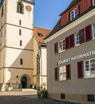 Tourist-Information neben einer Kirche mit Turm und roten Fensterläden. | © Stuttgart-Marketing GmbH, Sarah Schmid