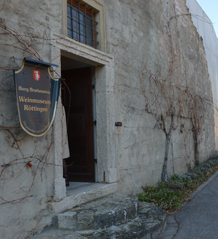 Blick auf den äußeren Eingangsbereich des Weinmuseums in Röttingen. An der Wand hängt ein großes Ritter-Schutzschild mit der Aufschrift "Burg Brattenstein, Weinmuseum Röttingen" . | © Stadt Röttingen