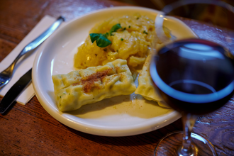 Ein Teller mit Maultaschen und Kartoffelsalat, daneben ein Glas Rotwein auf einem Holztisch. | © Kraichgau-Stromberg Tourismus e.V.