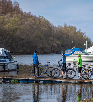 Radler stehen auf einem Steg auf dem Wasser und schauen sich Boote an. | © Thomas Gierth