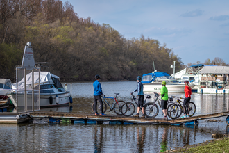 Radler stehen auf einem Steg auf dem Wasser und schauen sich Boote an. | © Thomas Gierth