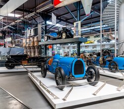 Zwei blaue Bugatti-Rennwagen aus den Anfängen des Automobils, ausgestellt in einem Museum mit weiteren historischen Fahrzeugen und Flugzeugteilen im Hintergrund. | © Technik Museum Sinsheim