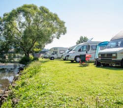 Mehrere Wohnmobile stehen auf einer Wiese neben einem Fluss, im Hintergrund ein großer Baum und Hügel. | © Landratsamt Rhein-Neckar-Kreis, Foto Dorothea Burkhardt