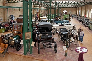 Großer Ausstellungsraum im Carl-Benz-Museum Ladenburg mit historischen Automobilen und Besuchern, sichtbare grüne Stahlträger und Backsteinwände. | © Landratsamt Rhein-Neckar-Kreis; Foto Dorothea Burkhardt