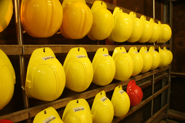 Mehrere gelbe Helme und ein roter Helm hängen in Reihen an einer Wand im Besucherbergwerk Schriesheim | © Landratsamt Rhein-Neckar-Kreis