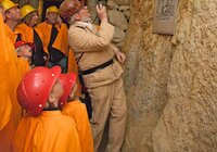 Gruppe von Personen in orangefarbener Schutzkleidung und roten Helmen in einem Stollen des Besucherbergwerks Schriesheim mit einem Führer, der auf eine Informationstafel an der Felswand zeigt. | © Landratsamt Rhein-Neckar-Kreis; Foto Dorothea Burkhardt