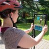 Frau mit orangefarbenem Helm hält Tablet, auf dem eine digitale Figur der Weitersehen App in einem Park angezeigt wird. | © Landratsamt Rhein-Neckar-Kreis; Foto Dorothea Burkhardt