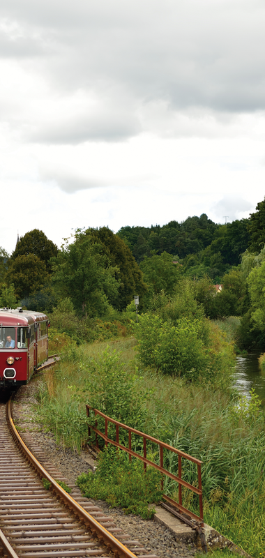 Roter Zug fährt auf Gleisen durch grünes Tal. | © Krebsbachtalbahn; Frank Jennerwein